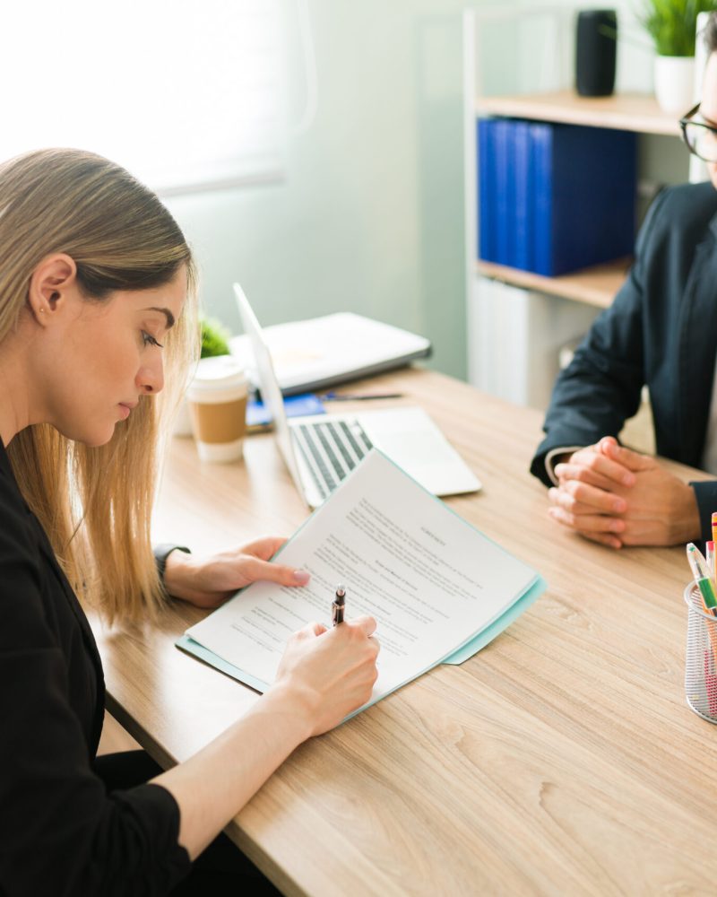 Beautiful caucasian woman signing a work contract to start a new job at a corporate office. Professional male boss making a business deal with a female client